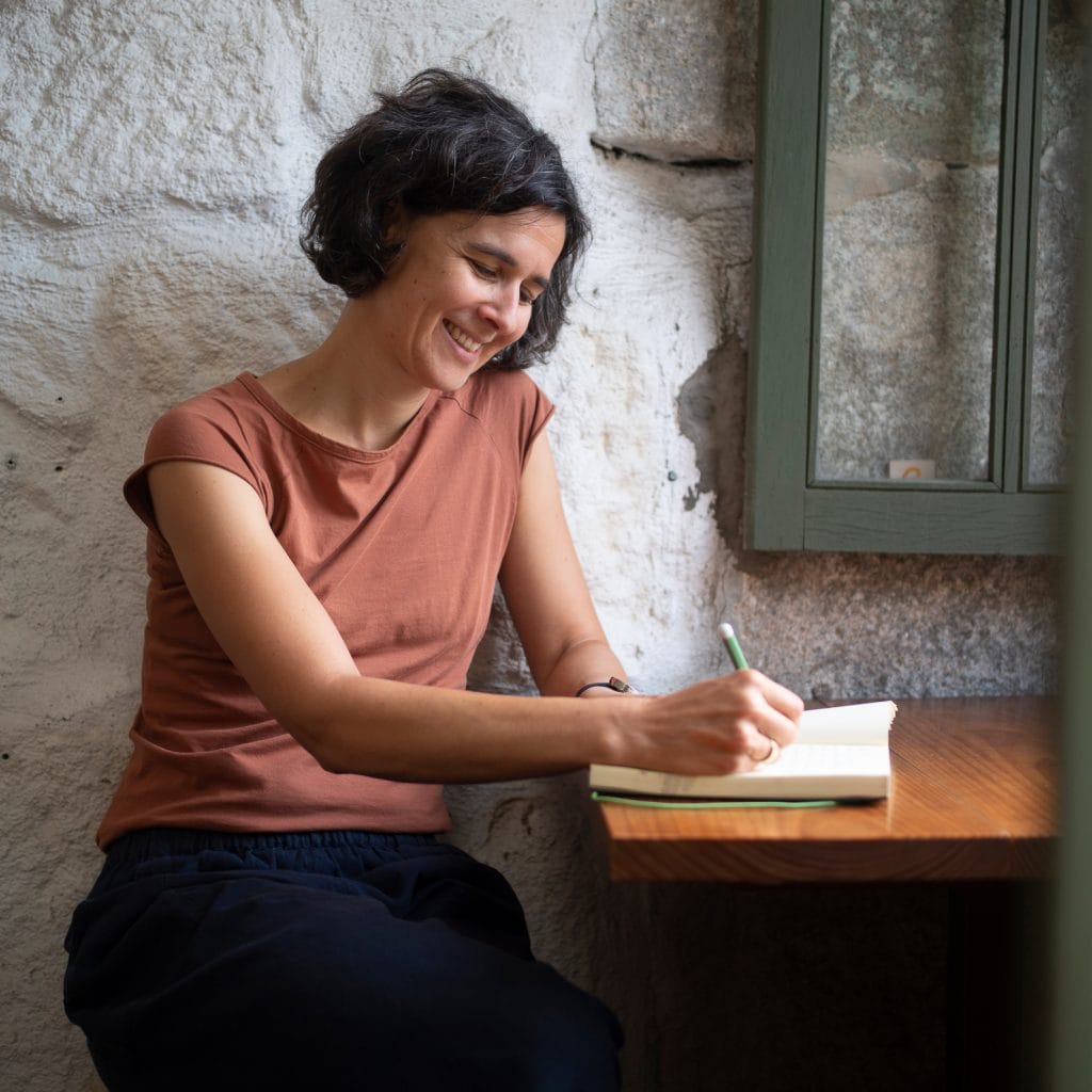 Barbara sitzt am Tisch und schreibt Ideen und Gedanken in ein Buch.